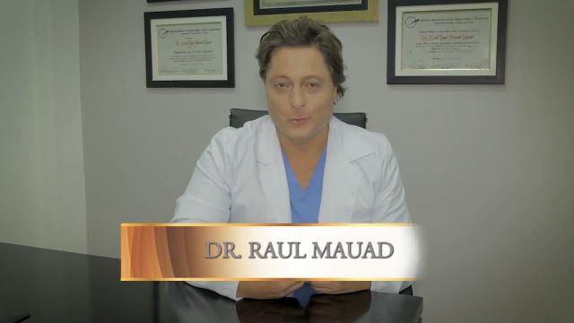 Imagem do Doutor Mauad de terno preto explicando alguma coisa em sua mesa de atendimento